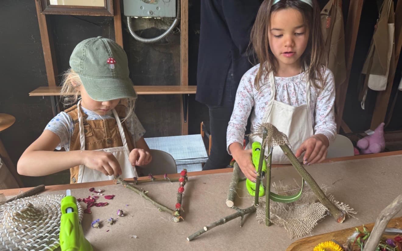 Two children building twig structures with natural materials and glue guns at MANA