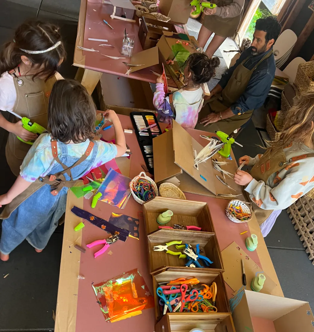 Children and a guide making cardboard creations with craft tools at MANA